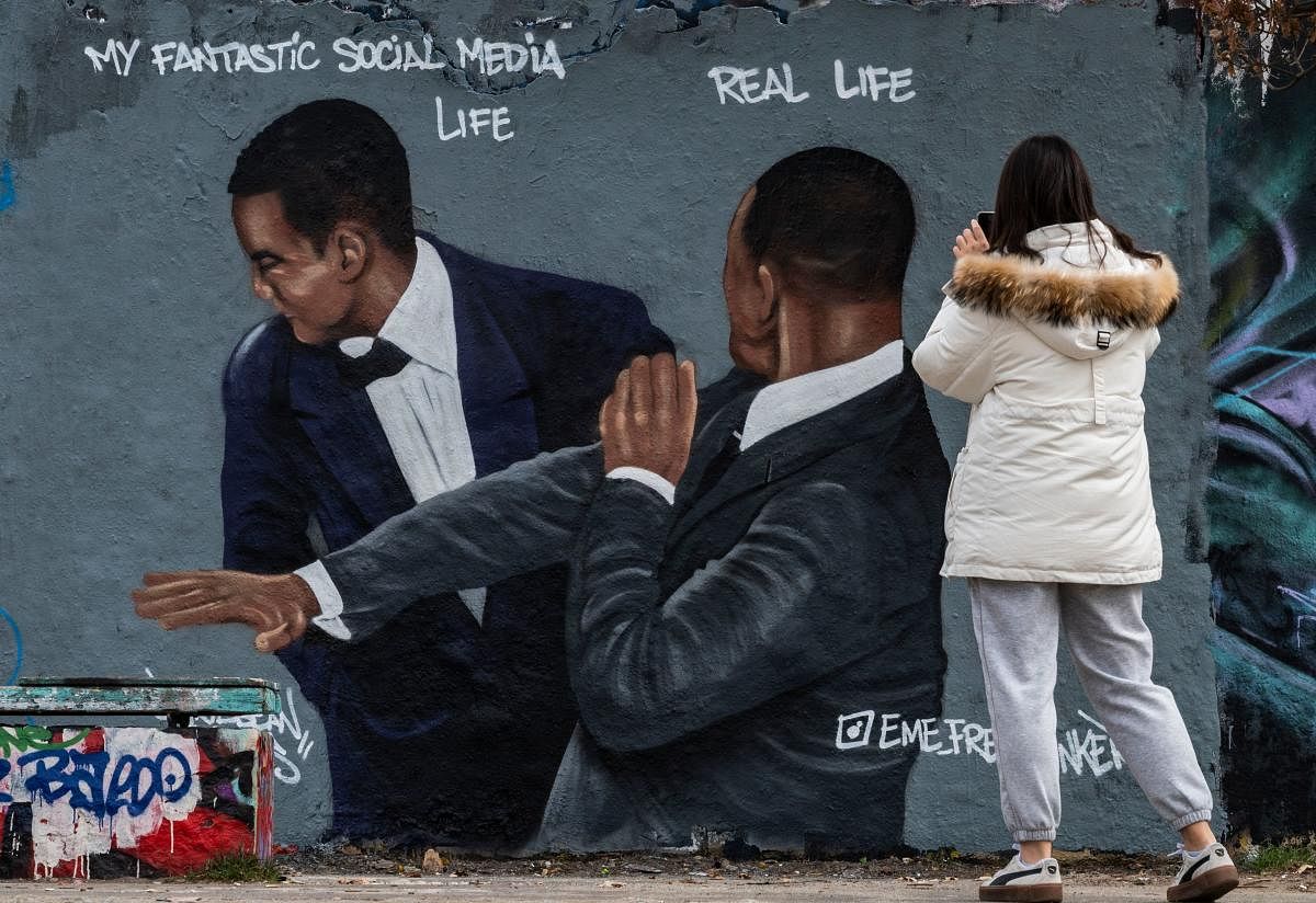 A woman takes a photo of a mural by Berlin-based street artist Eme Freethinker featuring the likeness of US actor Will Smith (R) slapping US comedian Chris Rock during the Oscars ceremony, in Berlin. Credit: AFP Photo