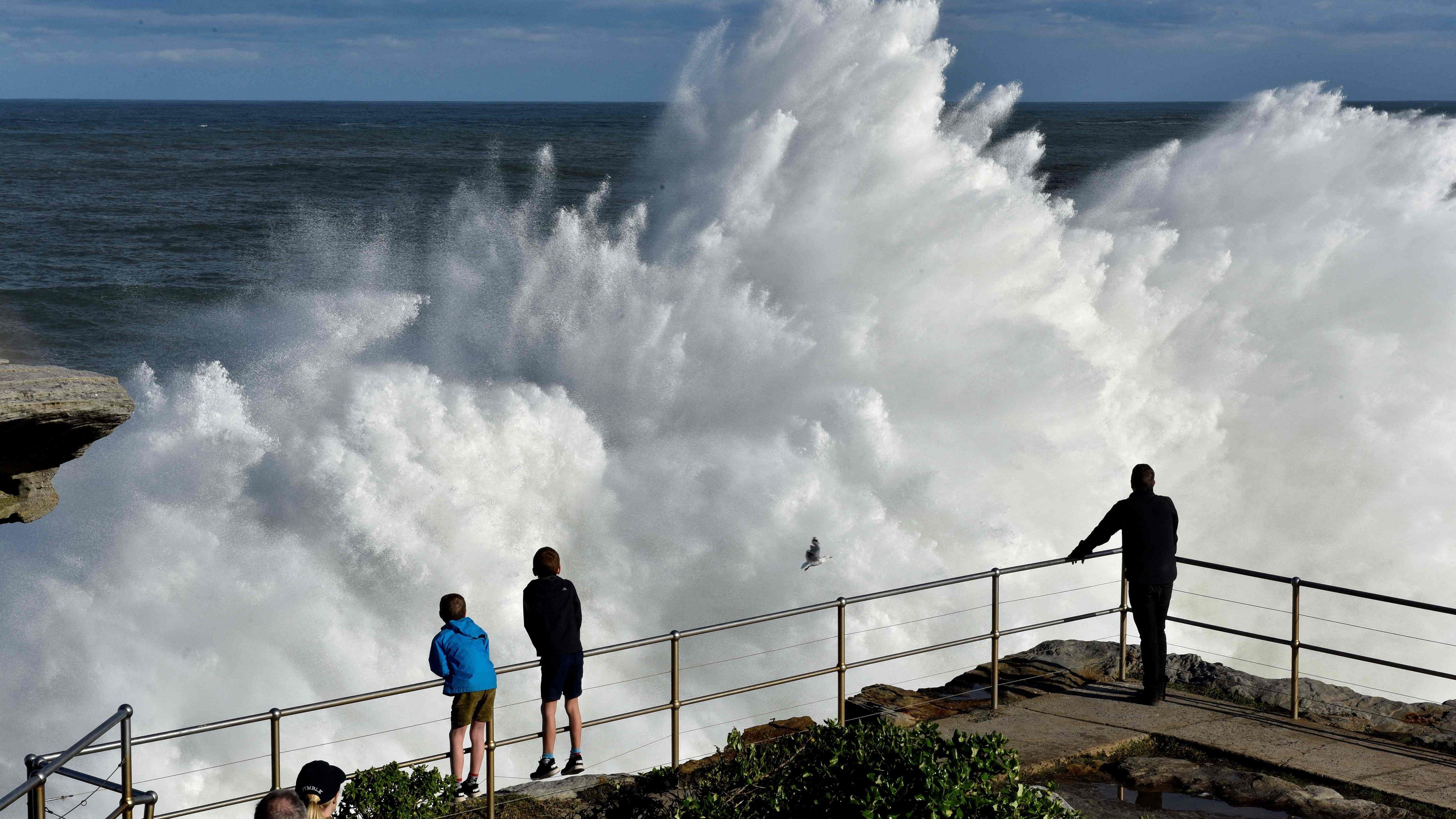 Residents watch a wave crashing into rocks at Bondi Beach in Sydney. Credit: AFP Photo