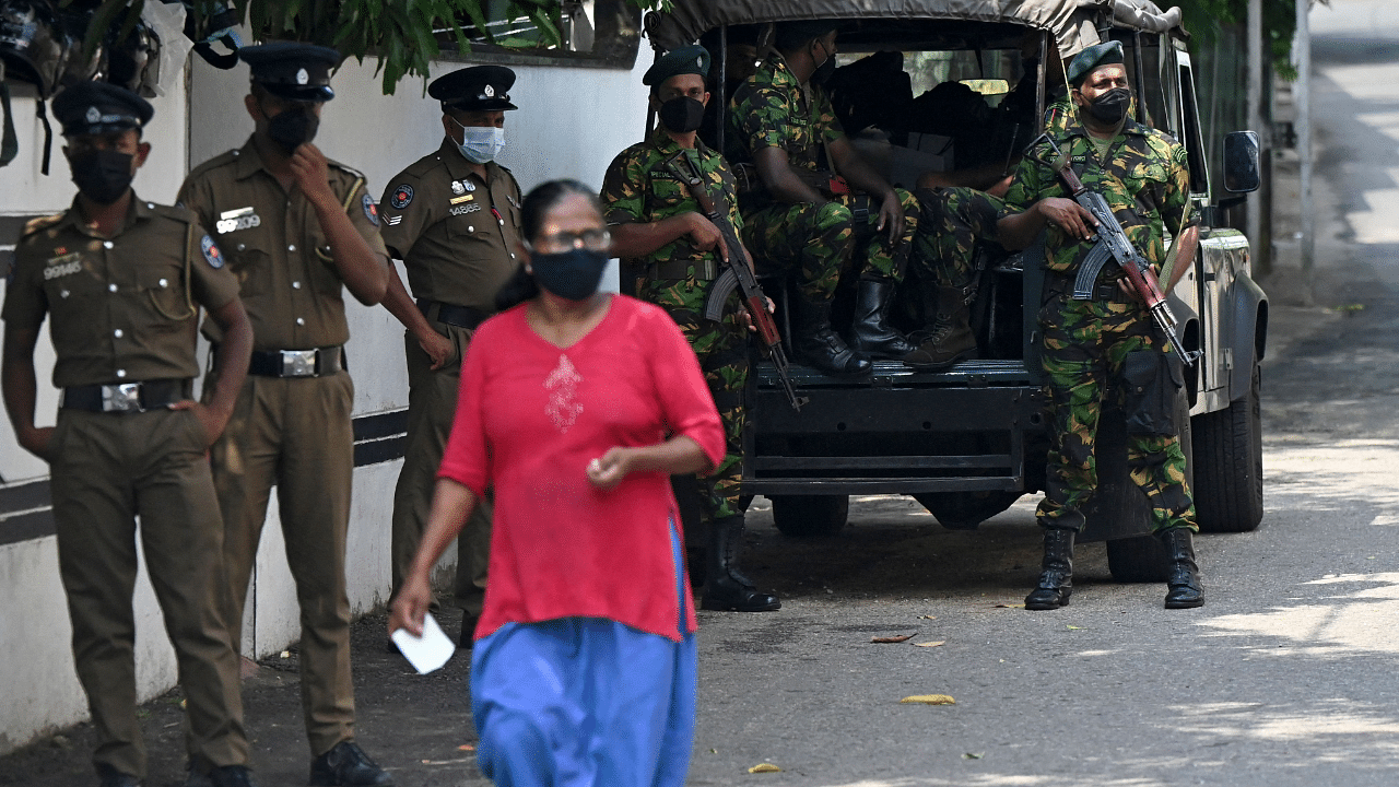 A pedestrian walks past Special Task Force (STF) and police personnel standing on guard along a street in Colombo. Credit: AFP Photo