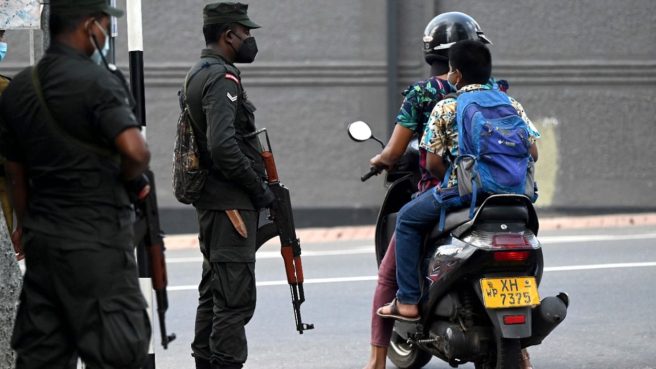 Commuters ride a scooter past soldiers standing on guard along a street in Colombo. Credit: AFP Photo