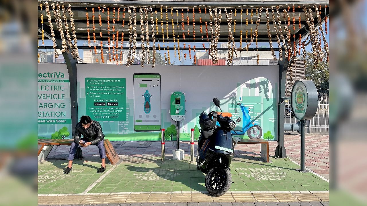 [Representational Image] A man checks his mobile phone as he waits while recharging his Ola electric scooter, in New Delhi. Credit: REUTERS FILE PHOTO