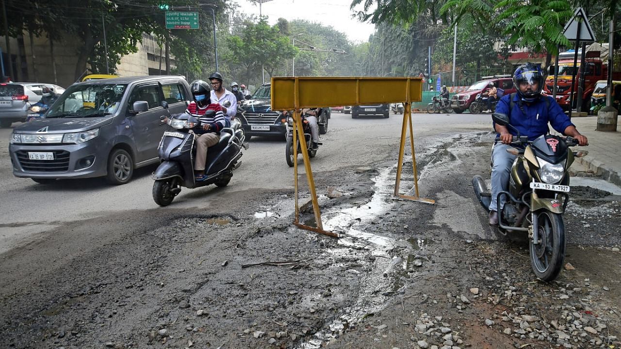Motorists struggle to navigate a pothole-filled stretch along Ambedkar Veedhi. Credit: DH Photo