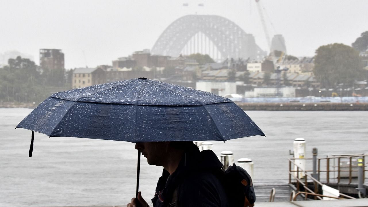 A man walks in front of the Harbour Bridge during rainfall in Sydney on April 7, 2022, as inclement weather triggered evacuation orders in several suburbs of Sydney's south and southwest. Credit: AFP Photo