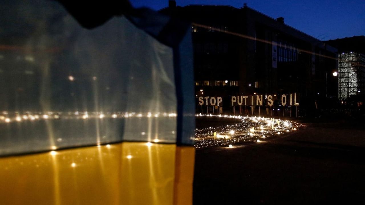 A demonstrator holds an Ukrainian flag in front of a sign reading "Stop Putin's oil" during a vigil for Ukraine near the European Union (EU) headquarters in Brussels, on March 22, 2022. Credit: AFP Photo