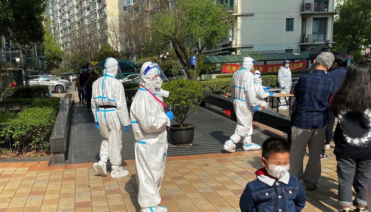 Medical workers in protective suits stand next to a line of residents waiting to take nucleic acid test at a locked down residential area, following the coronavirus disease (COVID-19) outbreak in Shanghai. Credit: REUTERS