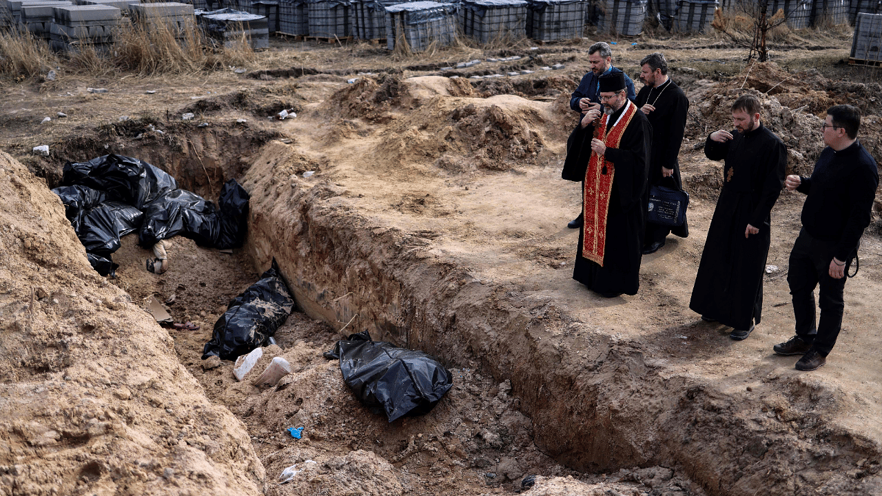 Priests pray at body bags in a mass grave in the garden surrounding the St Andrew church in Bucha. Credit: AFP Photo