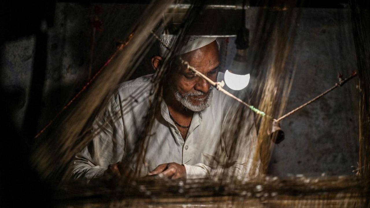 In this photograph taken on November 20, 2021, a worker uses a hand loom to weave a Banarasi silk sari at a workshop in Varanasi. Credit: AFP Photo