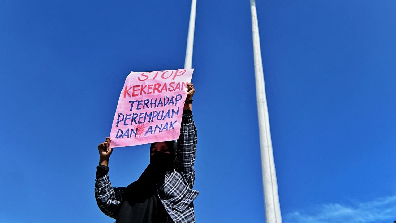 This photo shows a woman under an Indonesian flag holding a placard that reads "stop violence against women and children" during a protest against sexual abuse. Credit: Reuters File Photo