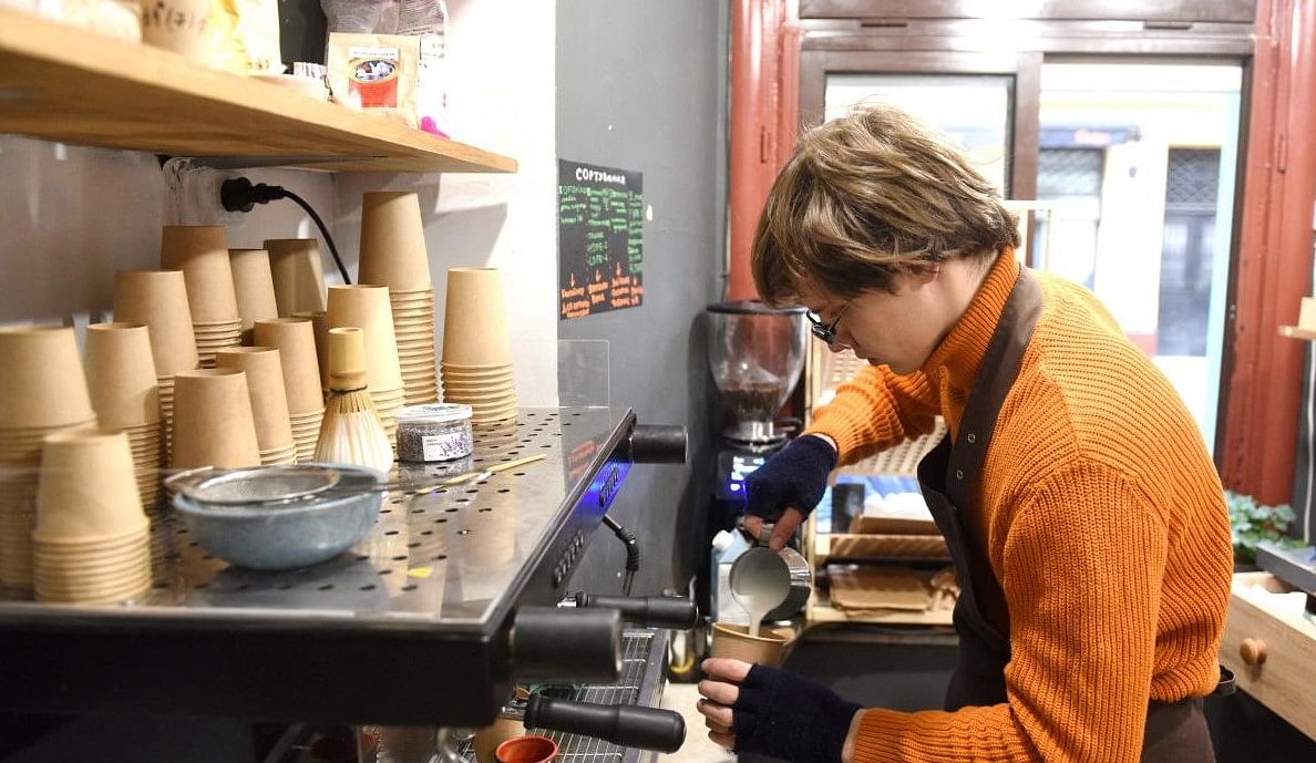 van Denchenko, 19, makes a drink at the Kiit cafe, in the western Ukrainian city of Lviv on April 12, 2022, amid Russia's military invasion launched on Ukraine. - After fleeing the capital, Denchenko and his friend Serhii Stoian started selling coffee from a ground-floor window in Lviv. Credit: AFP
