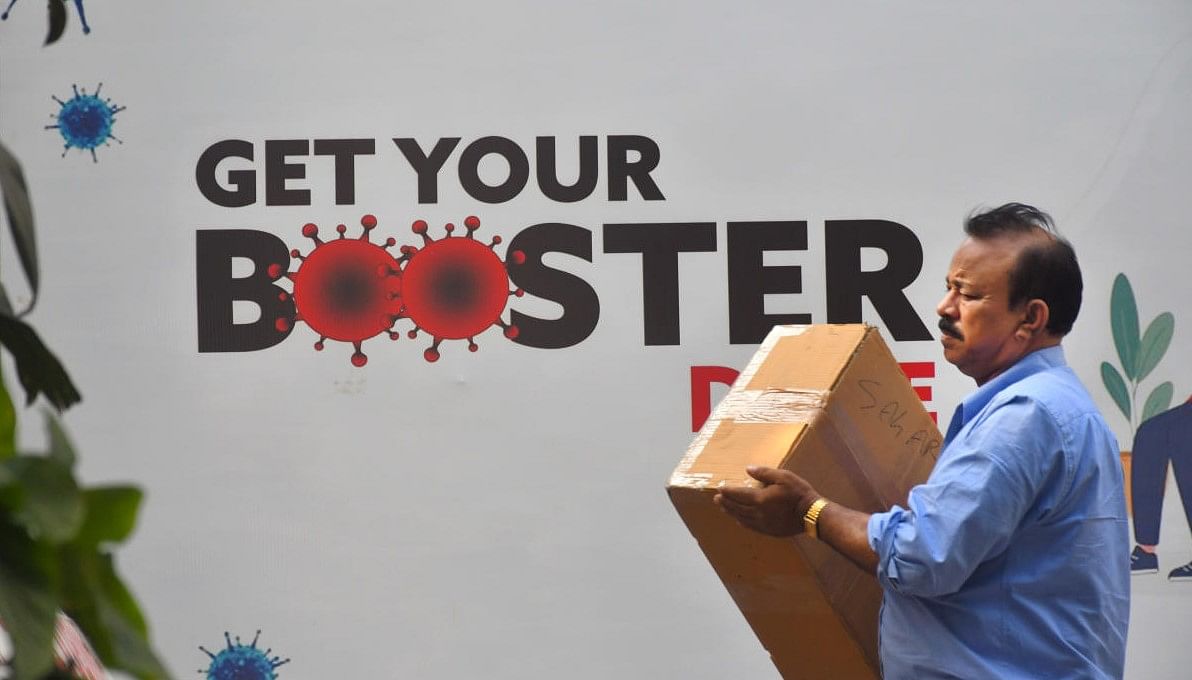 A man walks past a hoarding related to Covid-19 vaccine booster dose, outside a vaccination centre at Tilak Nagar, in New Delhi. Credit: PTI