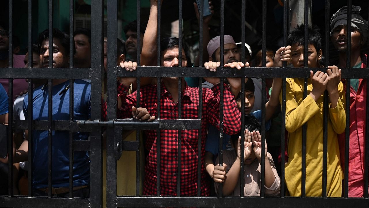 Residents stand behind a gate inside a lane while watching the demolition of illegal structures at Jahangirpuri in New Delhi. Credit: AFP Photo