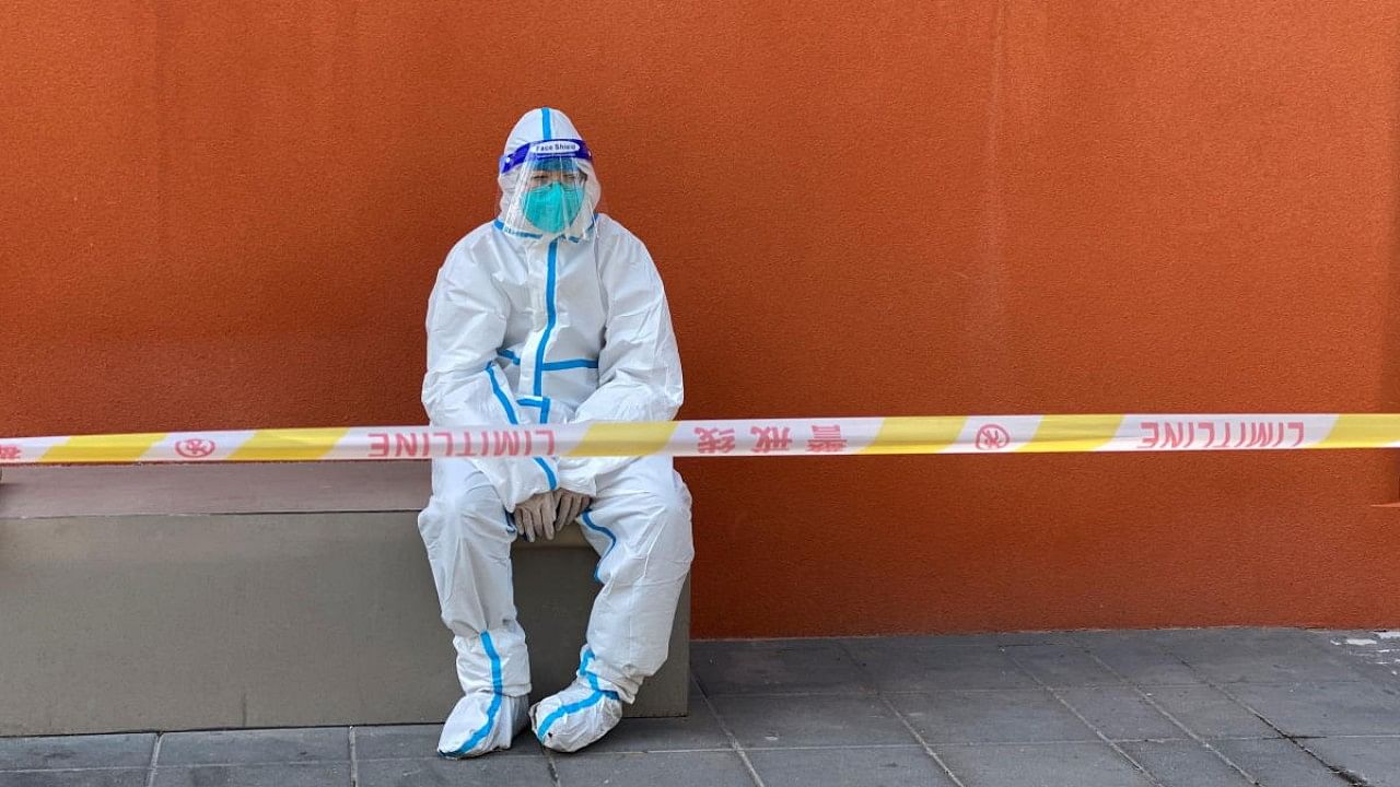 Worker in a protective suit sits near a police line outside a store, following the coronavirus disease outbreak in Shanghai. Credit: Reuters Photo