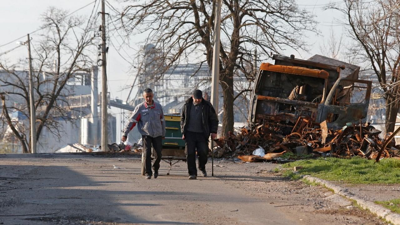 Local residents walk past a destroyed vehicle in Mariupol. Credit: Reuters Photo