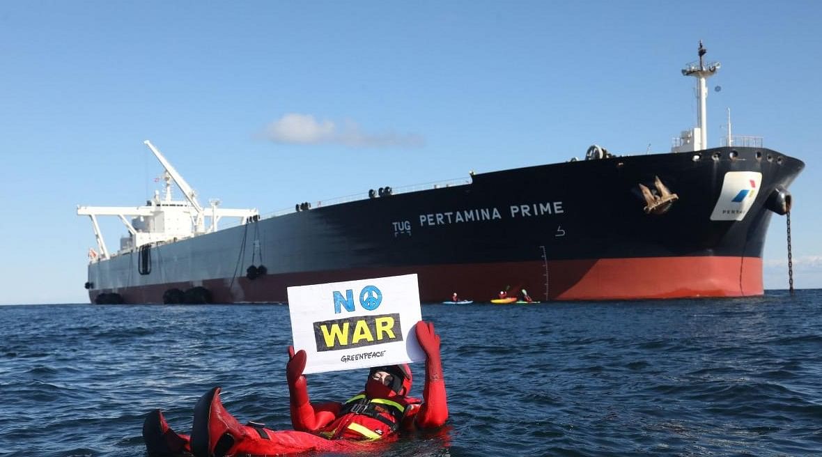 This Handout photo made available by Greenpeace shows one of their activists holding an anti-war placard as they float in the water in front of the supertanker Pertamina Prime off the coast of Denmark on March 31, 2022, blocking the transshipment of a Russian oil shipment between two ships. (Photo by Kristian Buus / GREENPEACE / AFP)