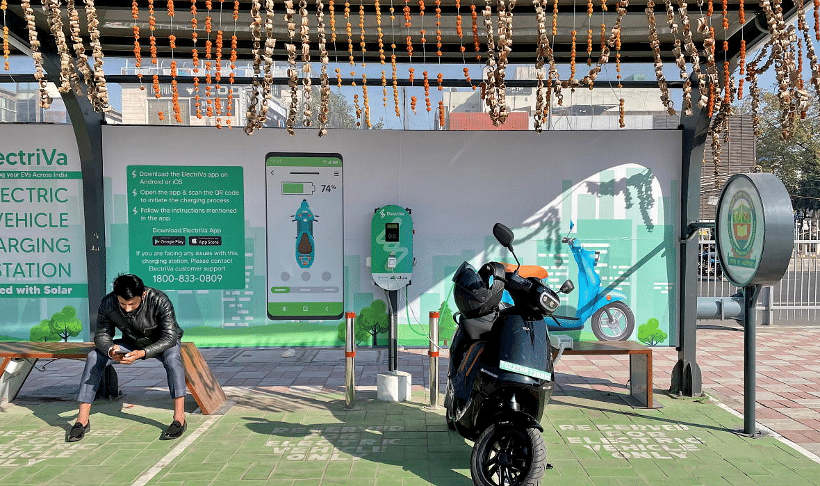 A man checks his mobile phone as he waits while recharging his Ola electric scooter. Credit: Reuters Photo