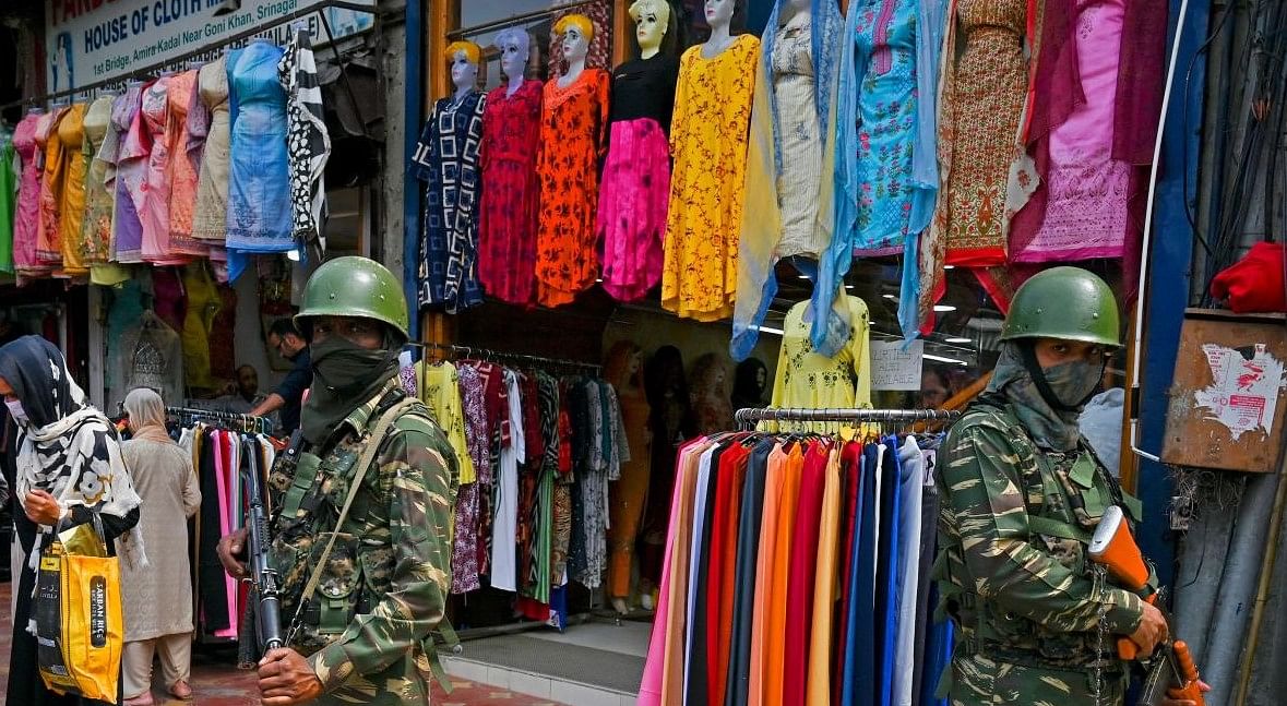 Indian paramilitary soldiers stand guard as people shop at a market for the Eid al-Fitr, which marks the end of the Muslim's holy fasting month of Ramadan in Srinagar on April 28, 2022. (Photo by TAUSEEF MUSTAFA / AFP)