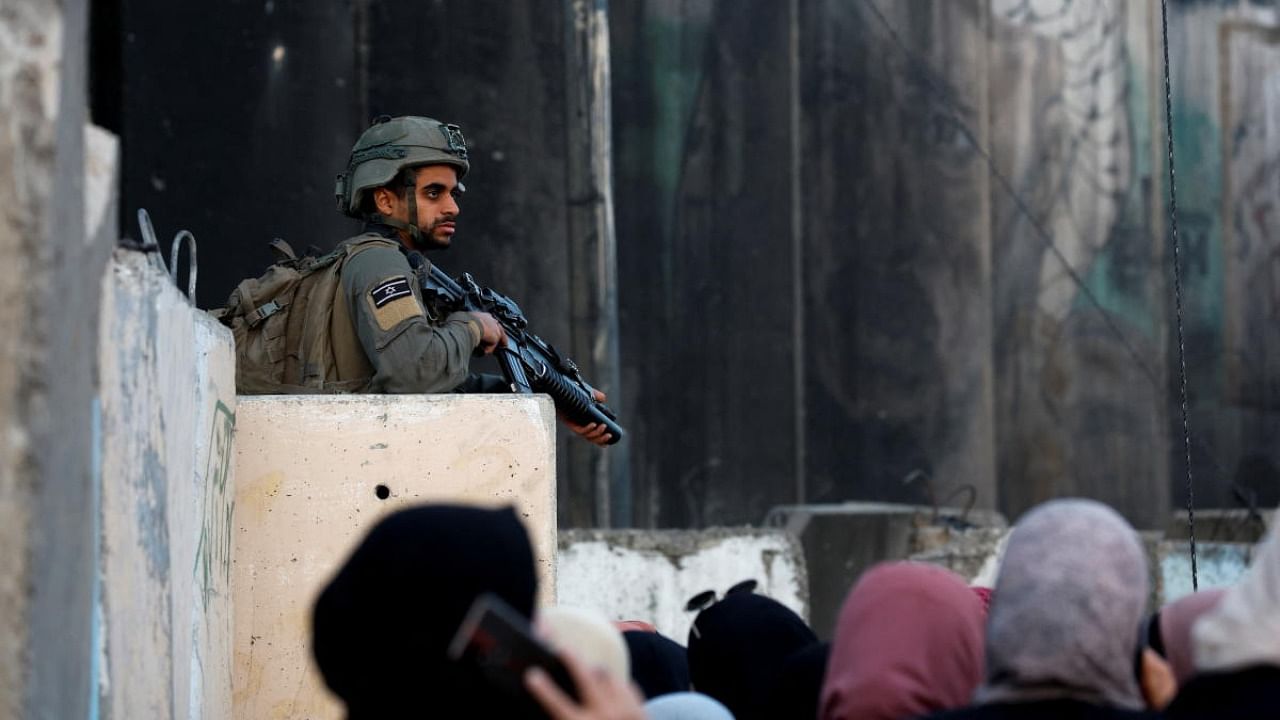 A soldier patrols as Palestinians make their way to attend the last Friday prayers of Ramadan in Jerusalem's Al-Aqsa mosque, at Qalandia checkpoint in the Israeli-occupied West Bank April 29, 2022. Credit: Reuters Photo