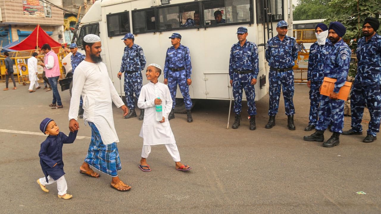 RAF jawans stand guard as a Muslim man walks with children on Eid-al-Fitr, in violence-hit Jahangirpuri area, in New Delhi. Credit: PTI Photo
