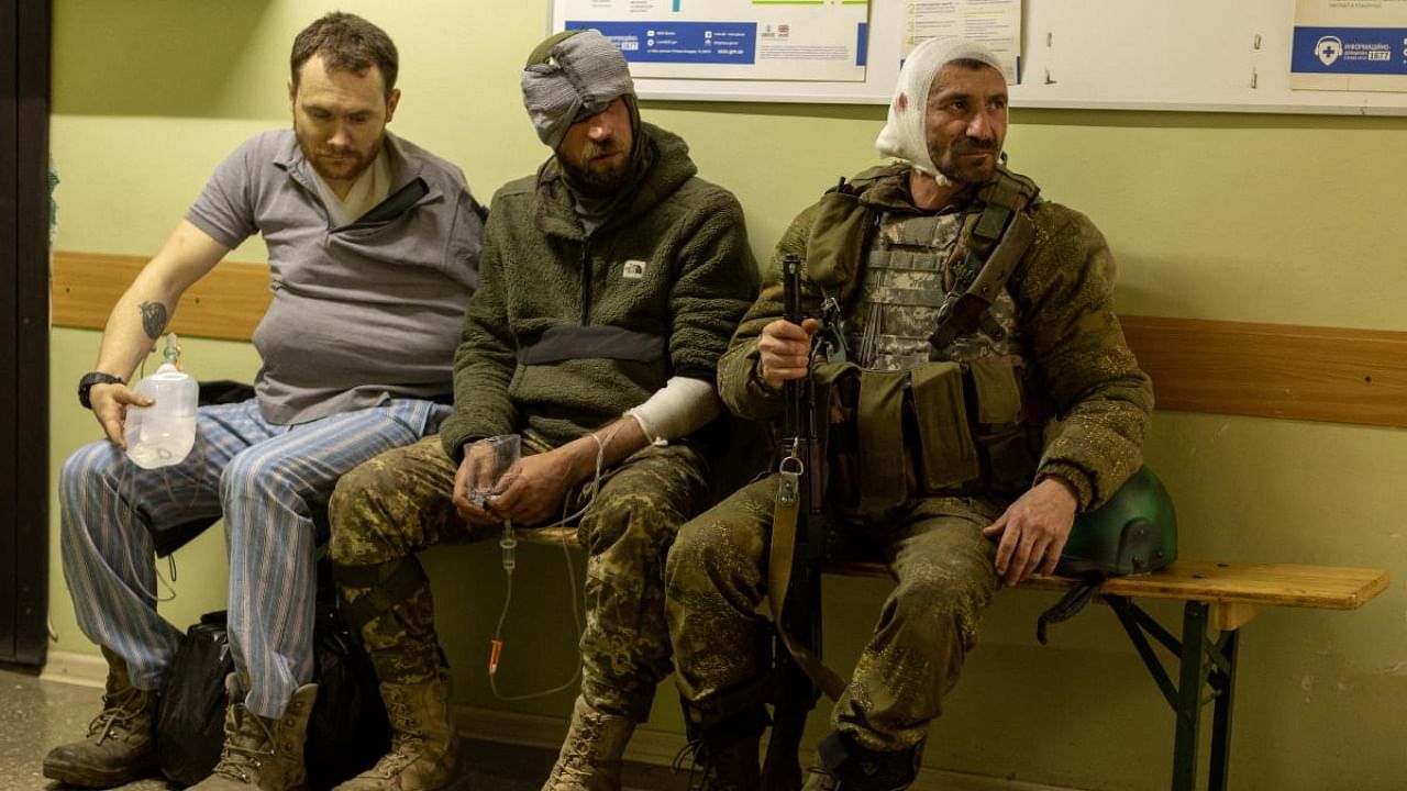 Injured Ukrainian volunteer soldiers, Maksim (C) and Andrei (R), sit on a bench in a hospital in Bakhmut, Donetsk region, Ukraine, May 5, 2022. Credit: Reuters Photo