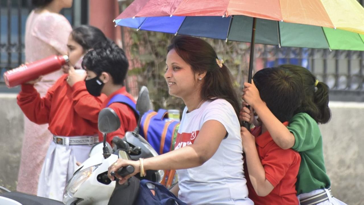 School students riding pillion on a scooter shield themselves under an umbrella from the sun on a hot summer afternoon, in Gurugram. Credit: PTI File Photo