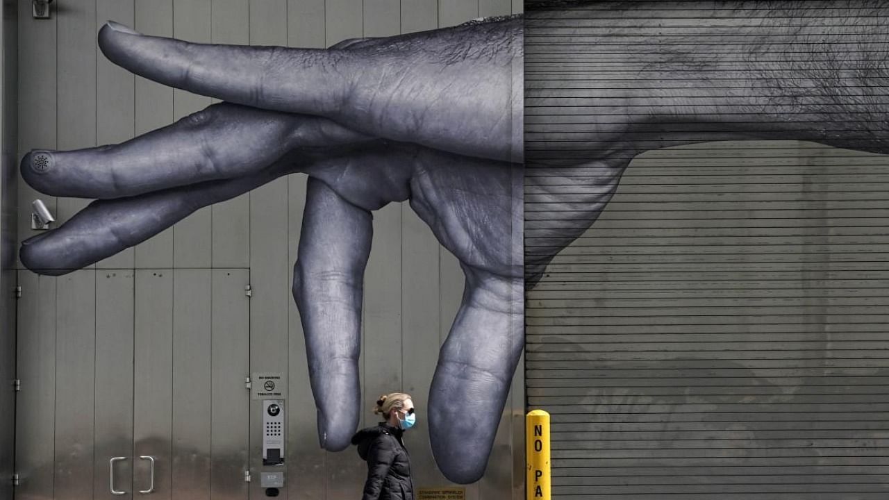  In this file photo taken on April 22, 2020, a woman in a mask walks past a mural of a hand by French artist JR on the side of a building in New York City. Credit: AFP Photo