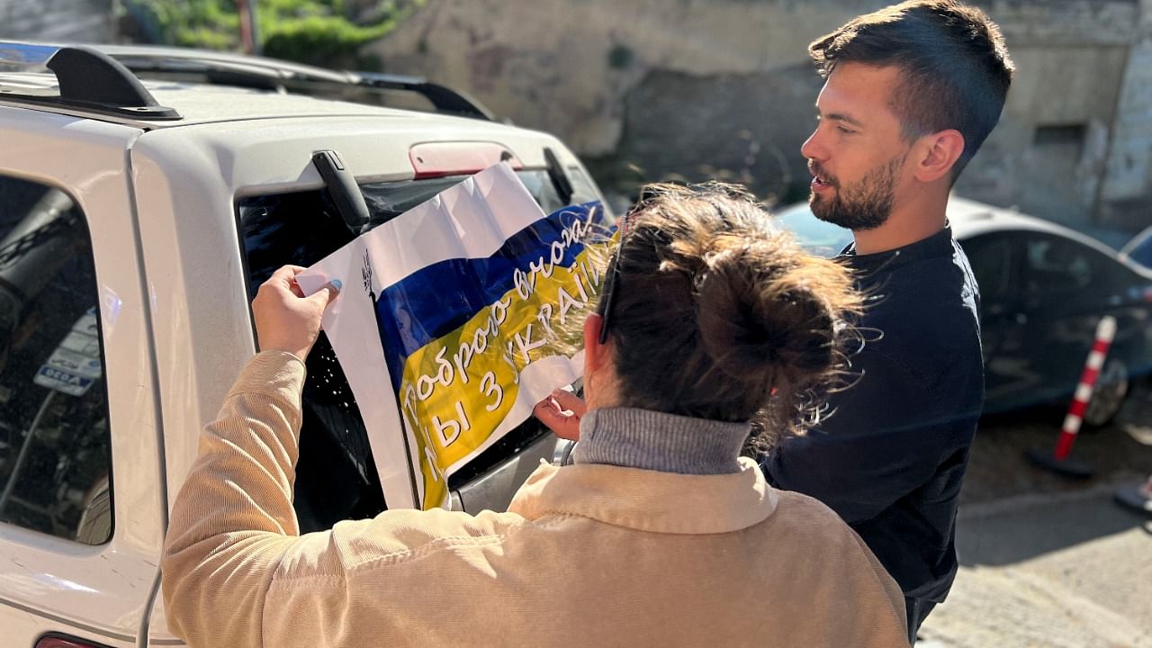 Maria Belkina and her partner Kirill Zhivoi, co-founders of Volunteers Tbilisi, a group which helps refugees from Ukraine, stick a sign with the Ukrainian flag onto a vehicle in Tbilisi. Credit: Maria Belkina/Handout via REUTERS
