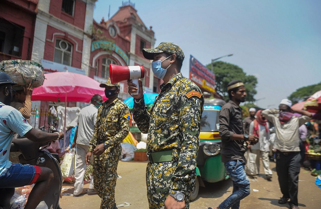 BBMP municipality marshals make announcements on a microphone for social distancing and wearing of masks, amid spread of coronavirus, at a city market in Bengaluru. Credit: PTI Photo
