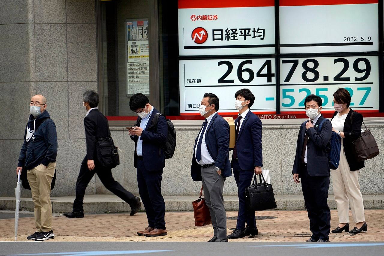 People wearing protective masks stand in front of an electronic stock board showing Japan's Nikkei 225 index at a securities firm Monday. Credit: AP Photo