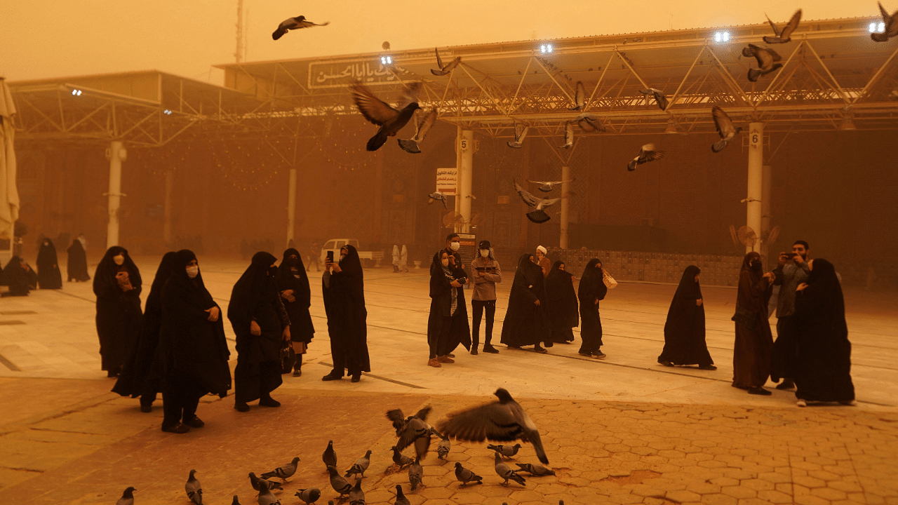 Visitors from Iran take pictures as they feed pigeons during a sandstorm in Iraq's holy city of Najaf. Credit: AFP Photo