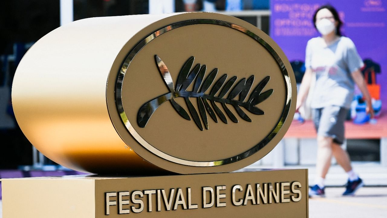 A woman wearing a protective face mask walks past an installation of a Palm d'Or symbol on the Croisette, on the day of the opening ceremony of the film festival. Credit: Reuters Photo