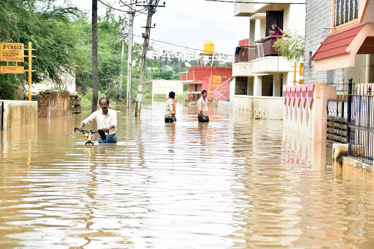 People wade through waist-deep water at Sree Sai Layout at Horamavu Agara following heavy overnight rain in Bengaluru on Wednesday. Credit: DH Photo