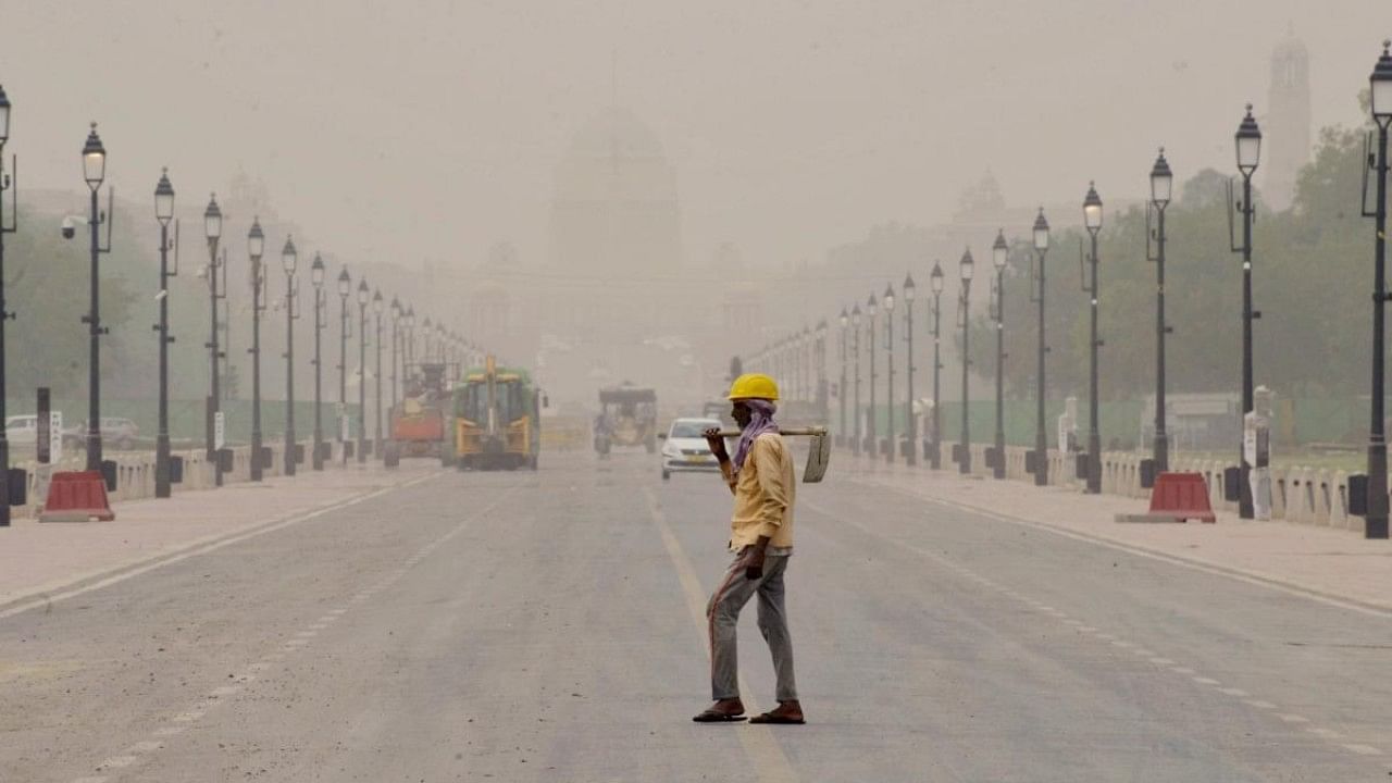A labour walks past at Rajpath during a mild dust storm in New Delhi. Credit: IANS Photo