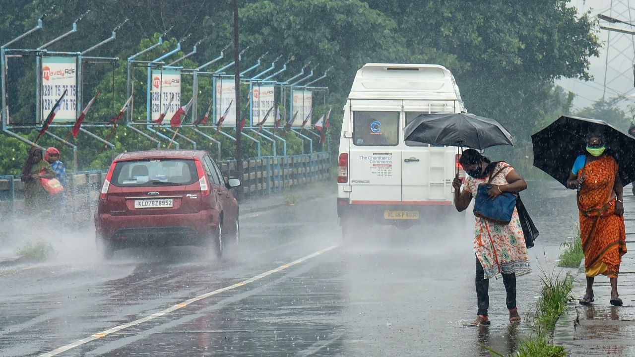 Pedestrians hold umbrellas as they walk on a roadside amid rainfall, ahead of the monsoon season, in Kochi. Credit: PTI Photo