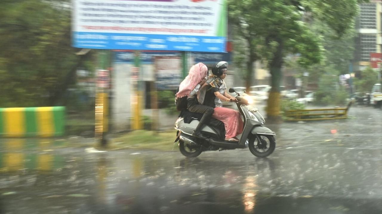 Commuters ride a scooter during rain in Ghaziabad, Monday, May 23, 2022. Credit: PTI Photo
