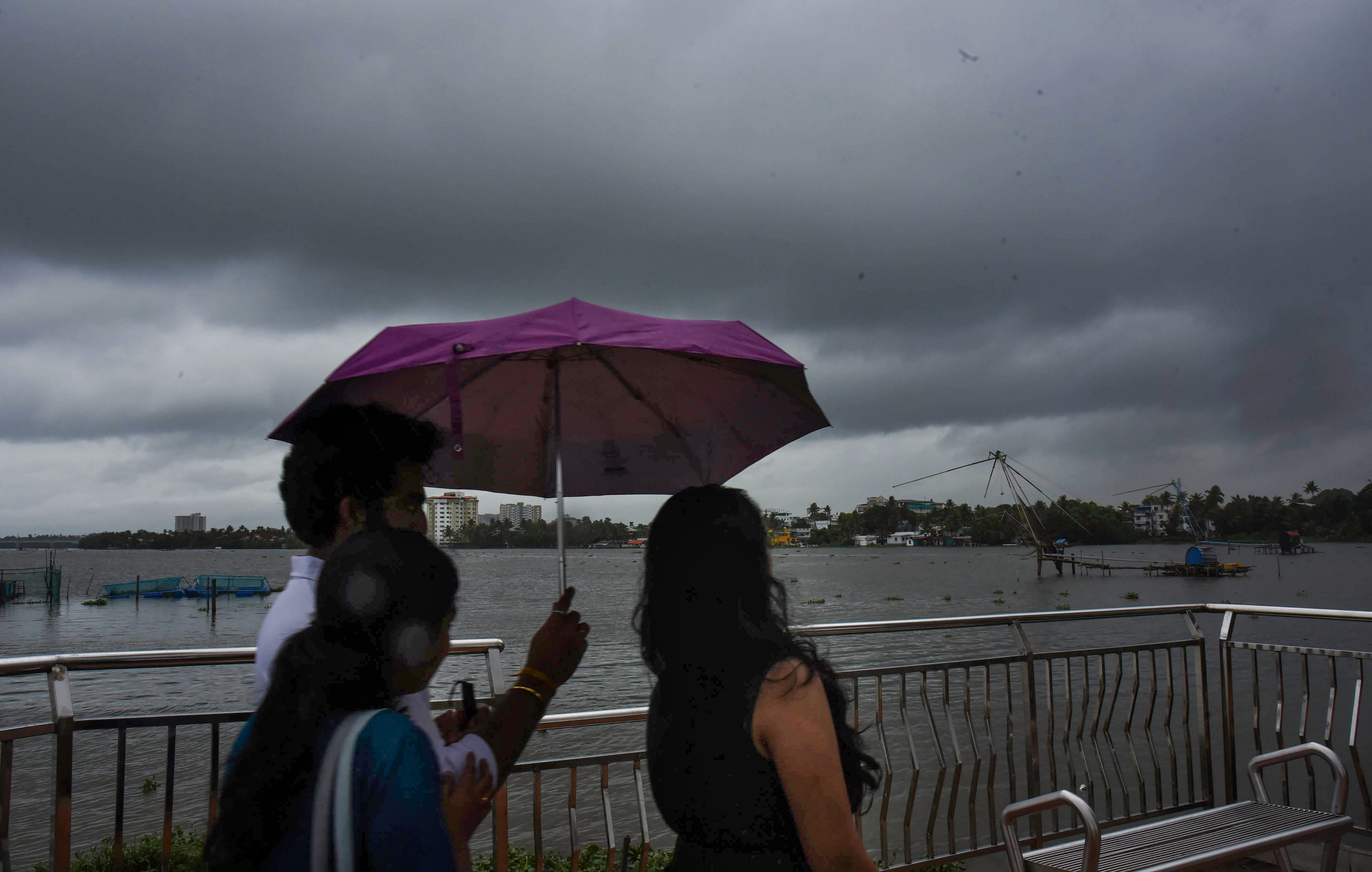 People use an umbrella to protect themselves from the rain, as dark clouds hover in the sky in Kochi. Credit: PTI Photo