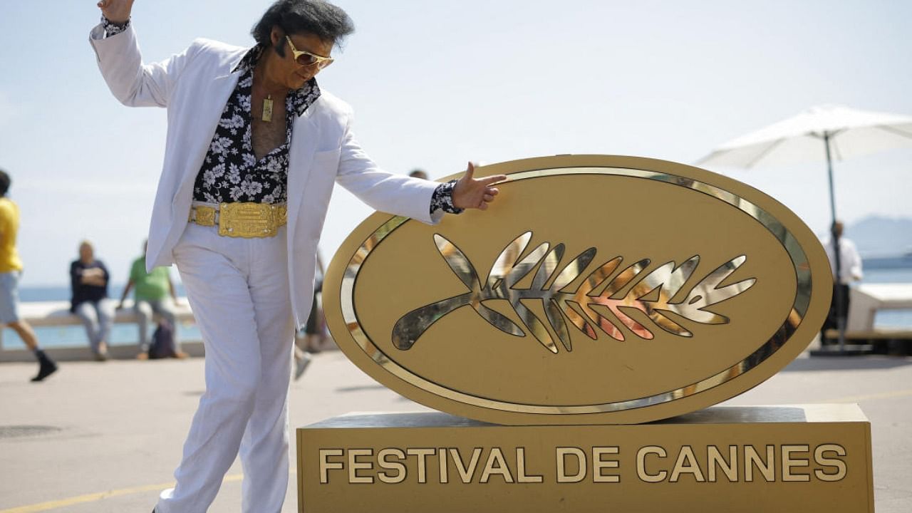Elvis Presley impersonator Eryl Prayer poses on the Croisette near an installation of a Palme d'Or symbol. Credit: Reuters Photo