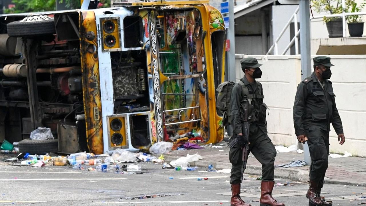 Sri Lankan soldiers walk past a burnt bus near Sri Lanka's former prime minister Mahinda Rajapaksa's official residence, a day after it was torched by protesters in Colombo on May 10, 2022. Credit: AFP Photo
