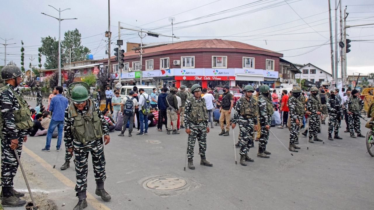 Security personnel stand guard as people from the Kashmiri Pandit community block a road to protest against the killing of the school teacher Rajni Bala, near Srinagar Airport. Credit: PTI Photo