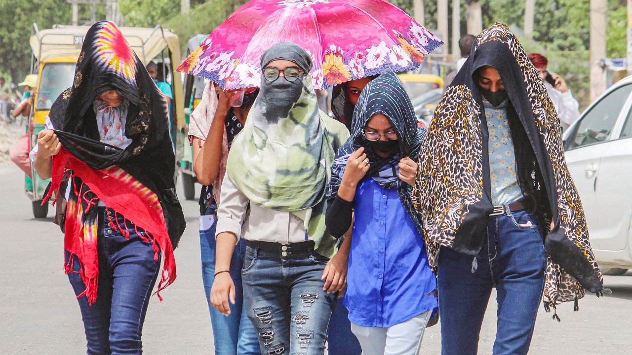 Women use scarves and an umbrella to shield themselves from the heat on a hot summer afternoon, in Gurugram. Credit: PTI Photo