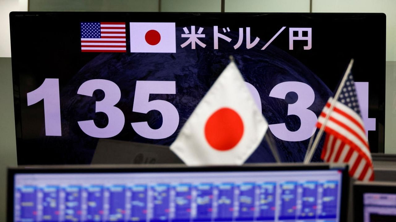 A monitor showing the Japanese yen exchange rate against the U.S. dollar is seen through the U.S. and Japanese national flags at the foreign exchange trading company Gaitame.com in Tokyo, Japan June 13, 2022. Credit: Reuters Photo
