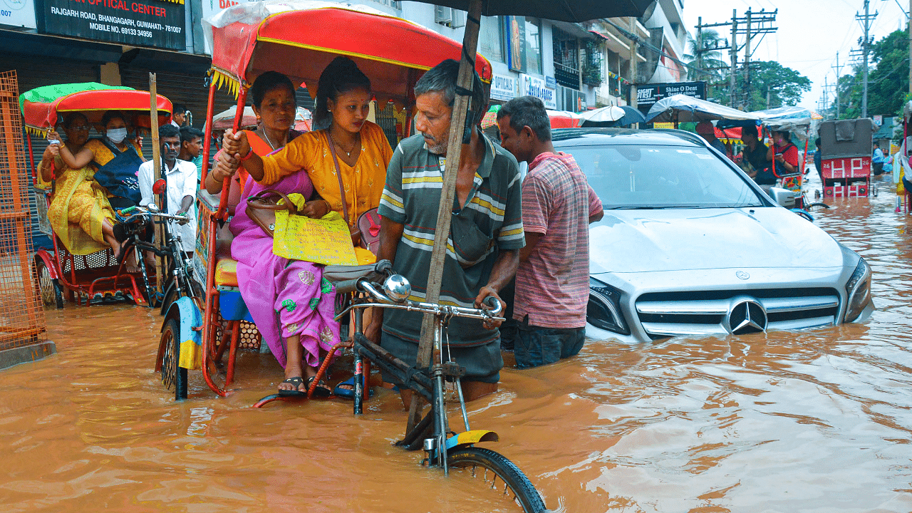 Rickshaw-pullers wade through a flooded street after rains, in Guwahati. Credit: PTI Photo
