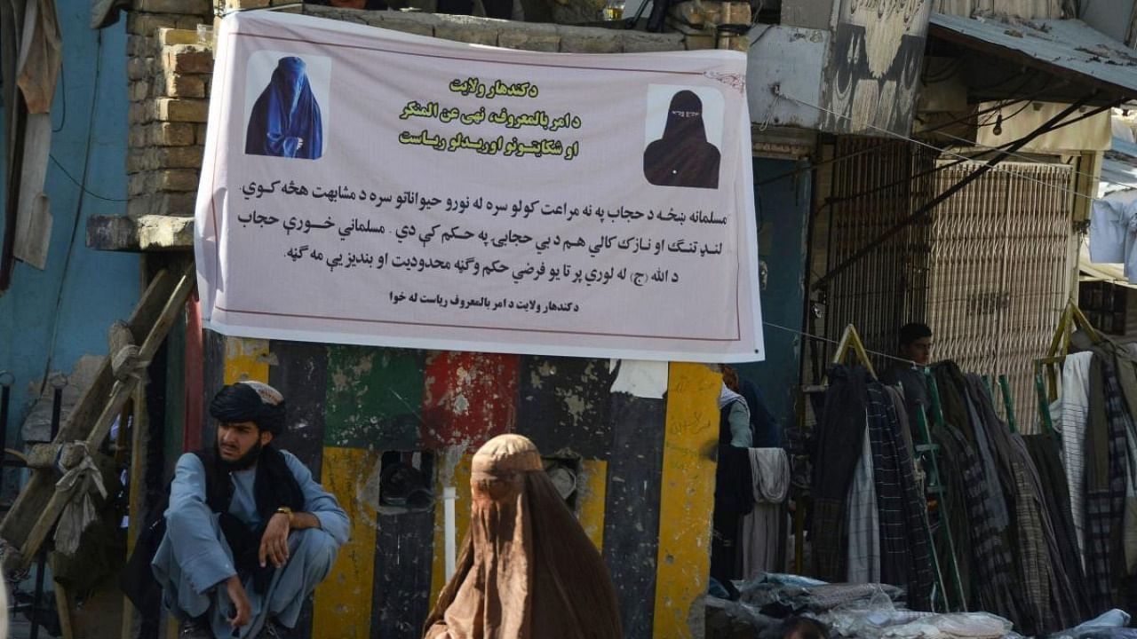 A burqa-clad woman walks past a banner placed by Taliban authorities asking women to wear a hijab, in Kandahar. Credit: AFP Photo