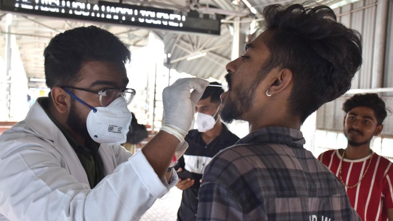 A health care worker collects swab samples from passengers for the RTPCR test at Yeshwantpur Railway Station in Bengaluru on Thursday. Credit: DH Photo