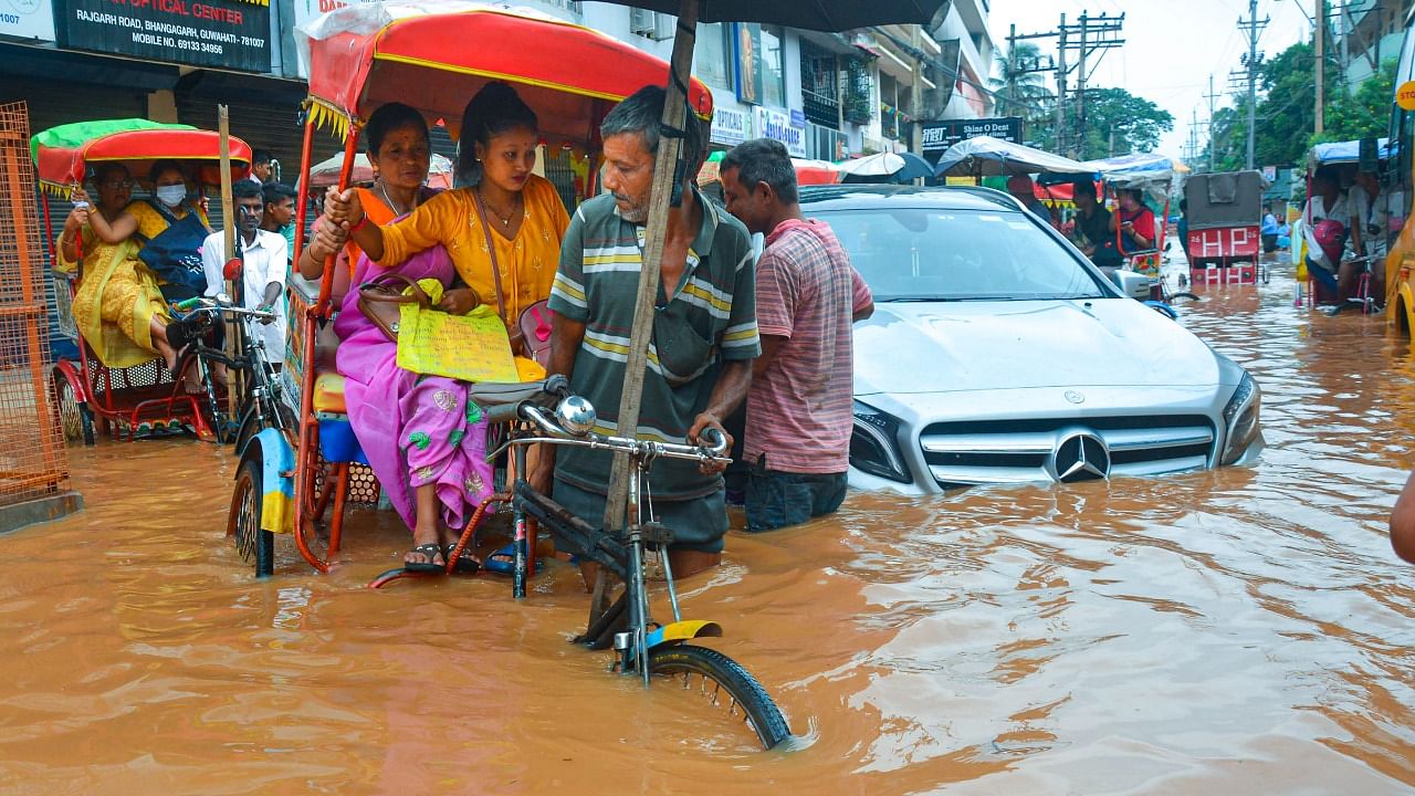 Rickshaw-pullers wade through a flooded street after rains, in Guwahati. Credit: PTI Photo