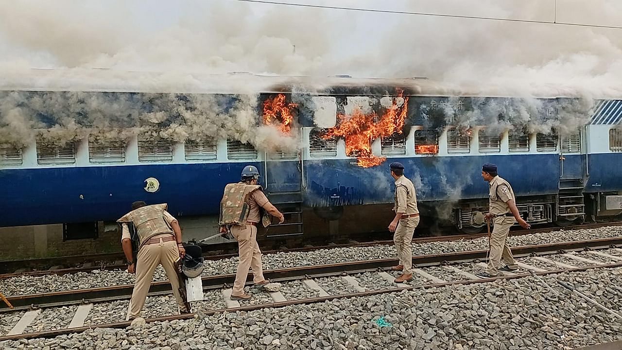 Policemen try to douse a fire in a train, set by people protesting against Centre's 'Agnipath' scheme. Credit: PTI Photo