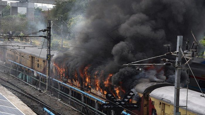 Smoke billows out from a passenger train coach after it was set on fire by protestors during a protest against Agnipath scheme. Credit: Reuters Photo