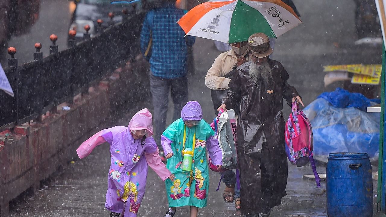 People use umbrellas and raincoats to shield themselves as they walk on a road amid rainfall, in Mumbai. PTI Photo
