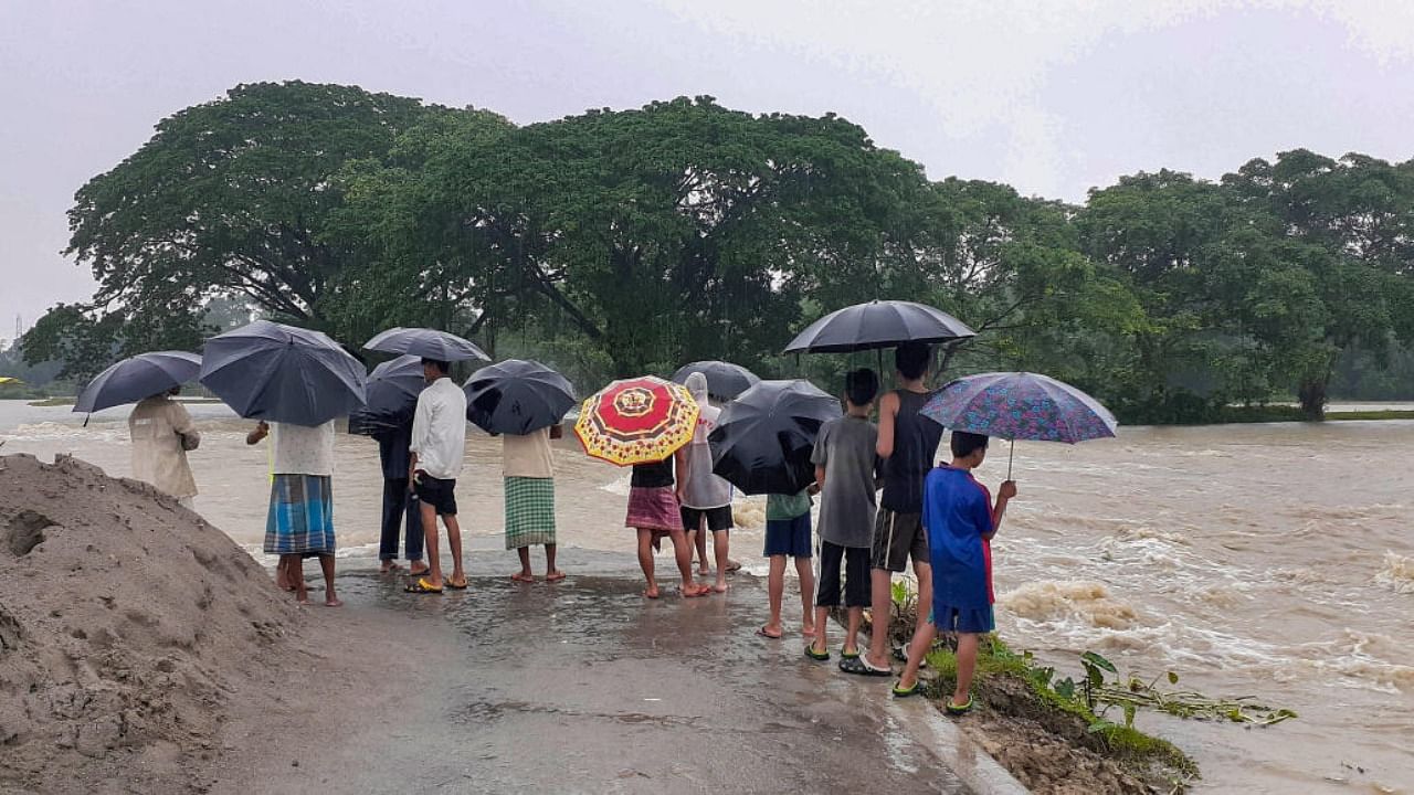 Flood-affected people stand on a road damaged by the flooded Pagladiya river, at Goalbil village, in Baksa district, Thursday, June 16, 2022. Credit: PTI Photo