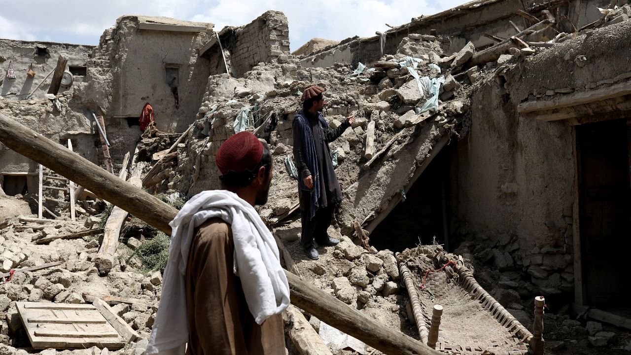 Afghan men stand on the debris of a house that was destroyed by an earthquake in Gayan. Credit: Reuters Photo