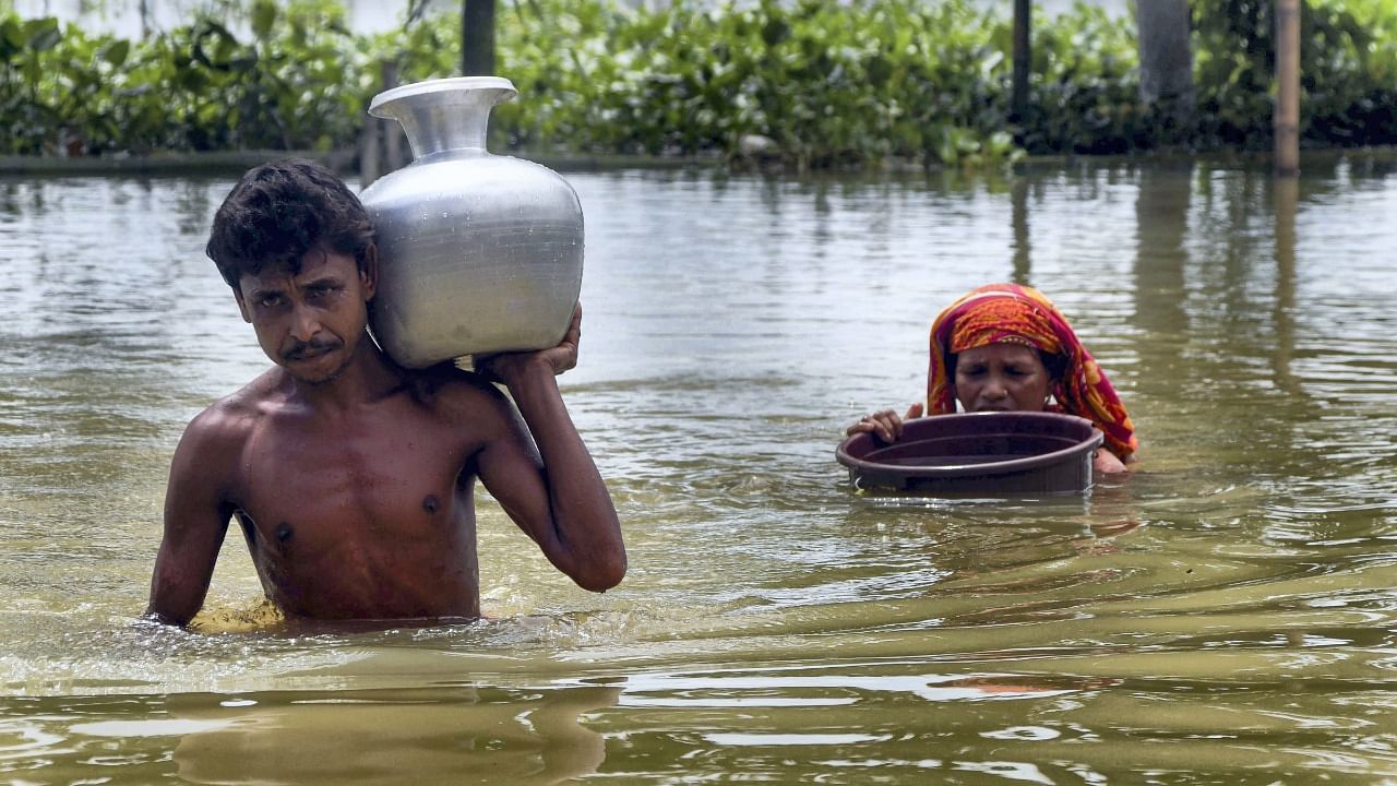 Villagers carry potable water in containers as they wade through a flooded area at Nilambazar village, in Karimganj district, on Friday. Credit: PTI Photo
